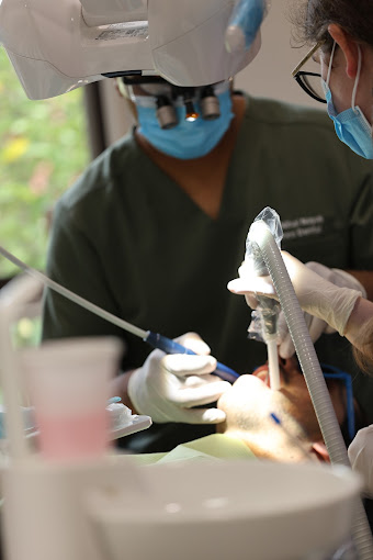 A dentist performing a procedure using advanced dental tools while an assistant provides support in a clinical setting